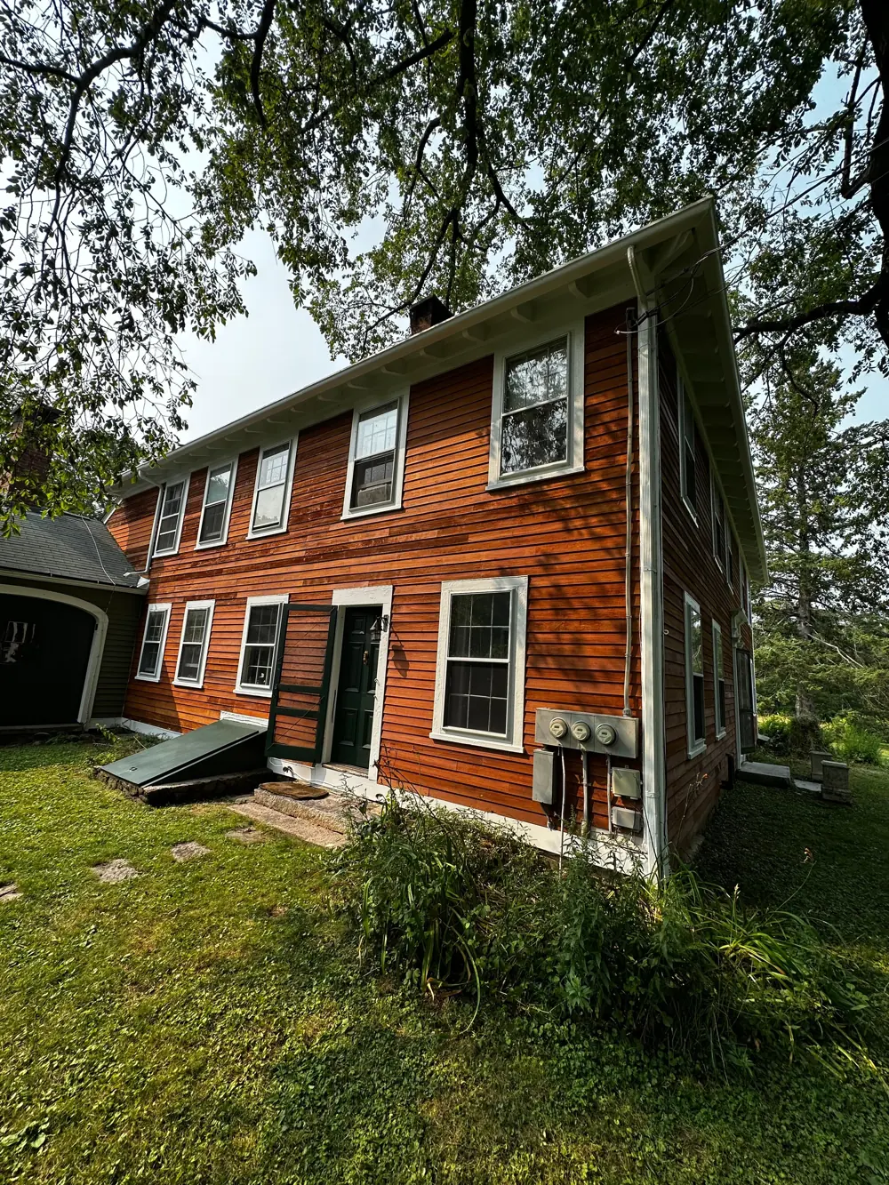 Side of a colonial house with red siding and white window trim